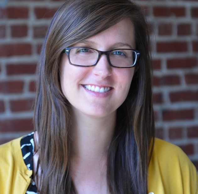 Headshot of a white woman with seeing glasses in a yellow  shirt.